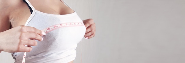 Young woman measures her breasts with a measuring tape