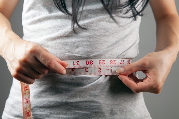 Young woman measuring belly with tape