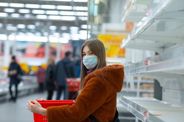 Giovane donna in maschera medica e scaffali vuoti in un supermercato