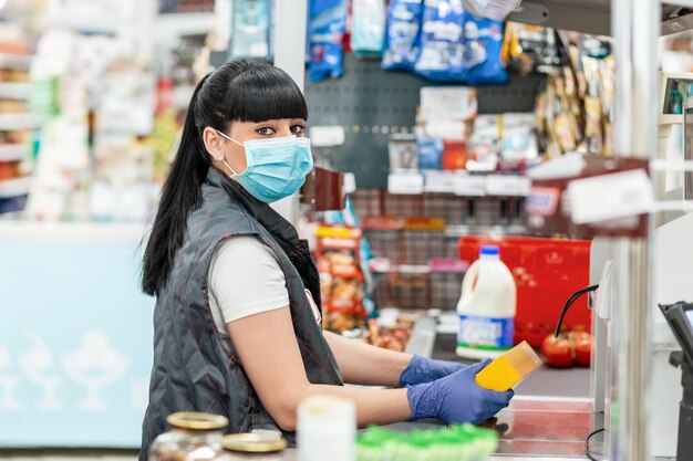 Foto una giovane donna con una maschera medica e guanti che lavora alla cassa in un supermercato concetto di coron