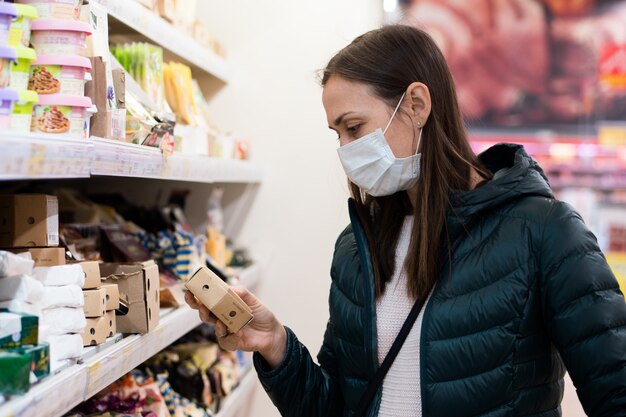 Молодая женщина в медицинской маске покупает молочную продукцию в супермаркете