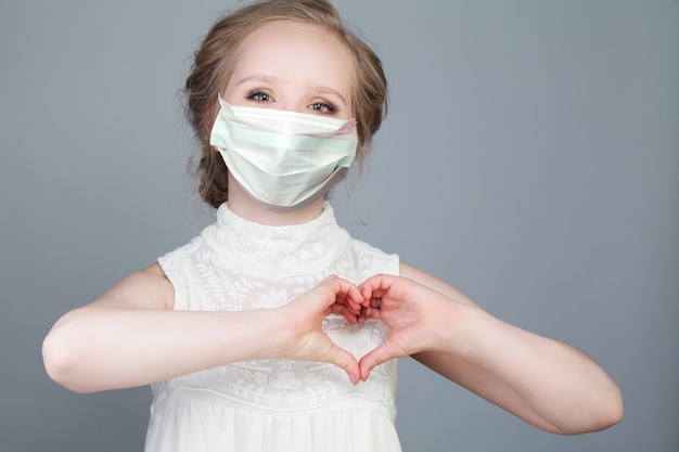 Young woman in medical mask making heart hang together