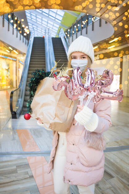 쇼핑몰에서 크리스마스 선물 쇼핑 의료 마스크에 젊은 여자