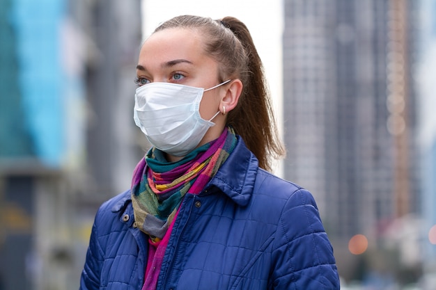 大気汚染と都市の流行のために路上で医療マスクの若い女性。ウイルス、感染、排気、産業排出物に対する保護