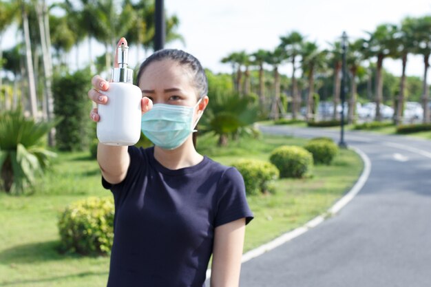 Young woman in medical protective mask and holding an alcohol in hand.