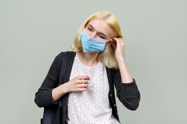 Young woman in medical protective mask. Teenager girl on green pastel background. Health care and protection, epidemics, youth concept