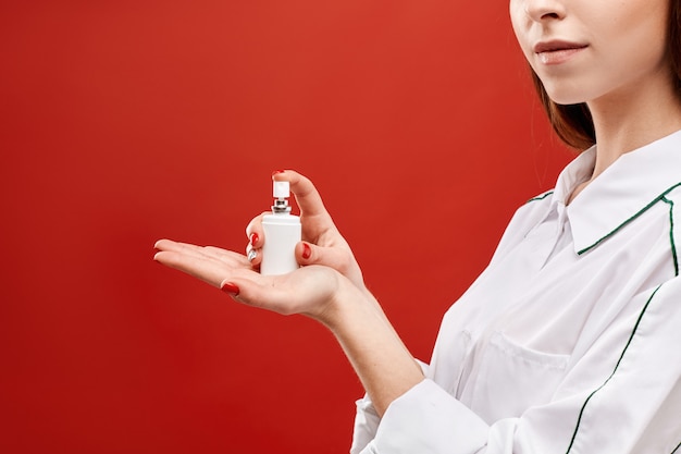 Young woman in medical uniform showing a spray jar with sanitizer at the red background,  Female doctor keeps a spray with medicine on her open palm