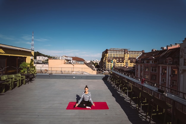 Young woman meditating in lotus pose at roof of the building