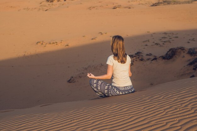 Young woman meditating in rad sandy desert at sunset or dawn