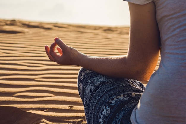 Молодая женщина медитирует в песчаной пустыне на закате