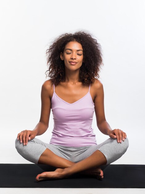 Young woman meditating while sitting on exercise mat against white background