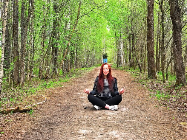 若い女性が森で頭の上にポットプラントを持って瞑想している