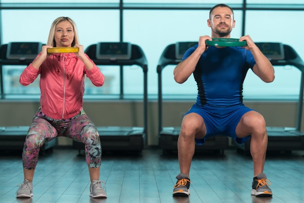 Молодая женщина и мужчины делают упражнения с весами в тренажерном зале