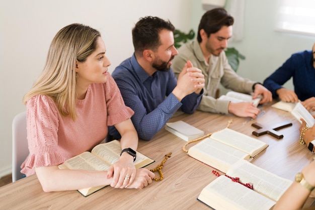 Young woman and men paying attention to the talk of a member of a bible study group before starting their catholic prayers