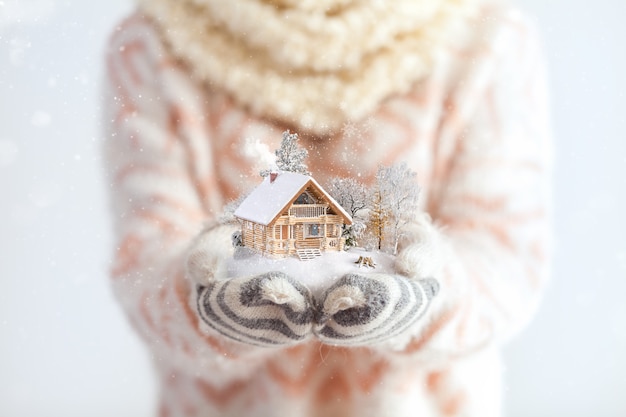 Young woman in mittens holding snow in her hands with a log house. Unusual christmas concept