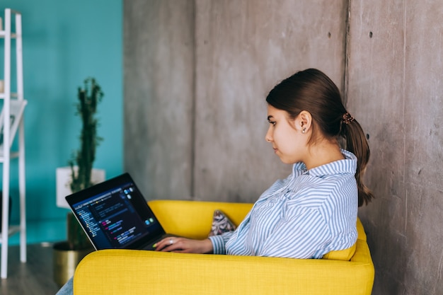 Young woman mobile developer with laptop, writes program code on a computer, programmer work in modern office.