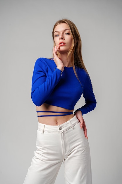 Young woman model in blue top and white pants posing on white background