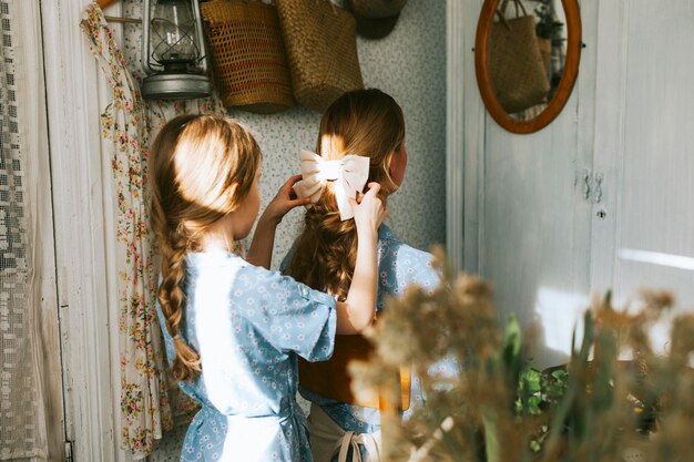 写真 若い女性と彼女の小さな娘は,家族の見た目で,ドレスを着て,春のテラスで花を植えています. 家の庭園で,苗木を育てています. 田舎の家,ベランダ. 母性は,お互いに型の弓をします.