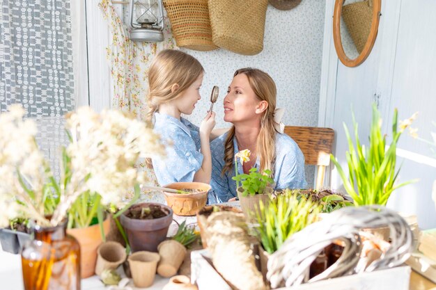 写真 若い女性と彼女の小さな娘は家族の見た目でドレスを着て春のテラスで花を植えています家庭の庭園で苗が育つ田舎の家ベランダ母性