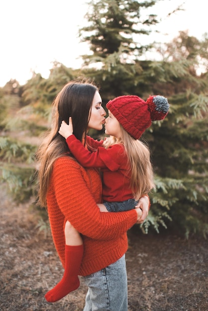 Young woman mom spend time with daughter kid girl wear red knit sweater and hat over tree outdoor Motherhood Autumn season