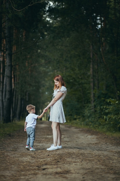 Young woman mom walks with little baby son in the woods hand teaches to walk