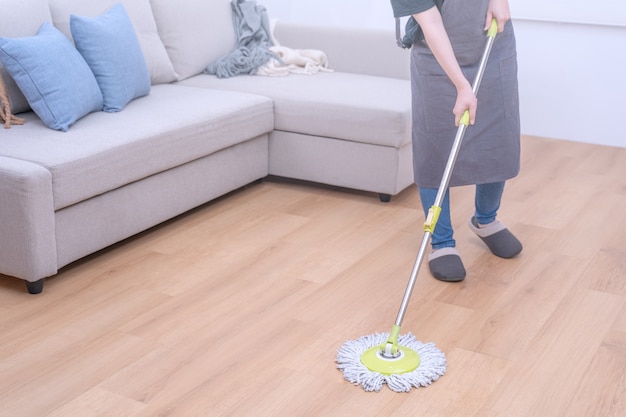 Young woman mopping wooden floors at home with a mop