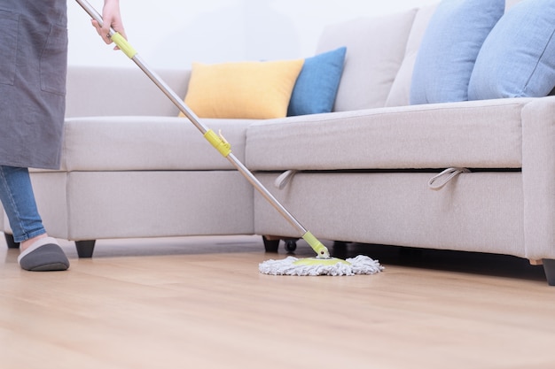 Young woman mopping wooden floors at home with a mop