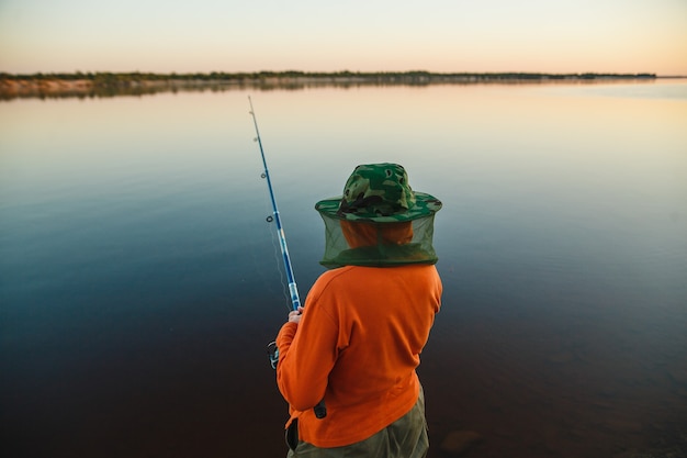 Young woman in mosquito net fishing with fishing rod in the evening