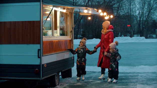 A young woman mother with her children walking to a little shop on skates