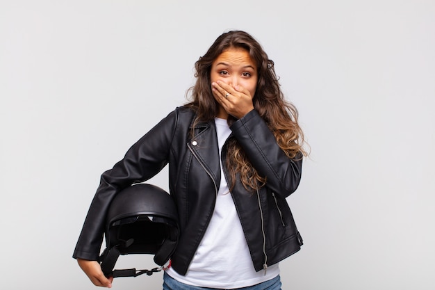 Young woman motorbike rider covering mouth with hands with a shocked, surprised expression, keeping a secret or saying oops