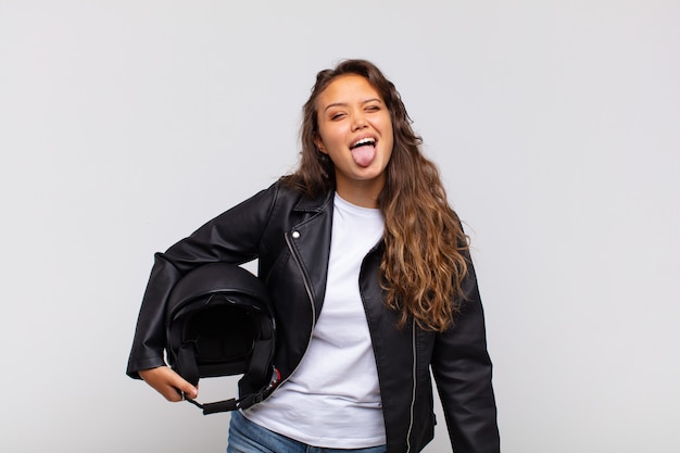 Young woman motorbike rider with cheerful, carefree, rebellious attitude, joking and sticking tongue out, having fun