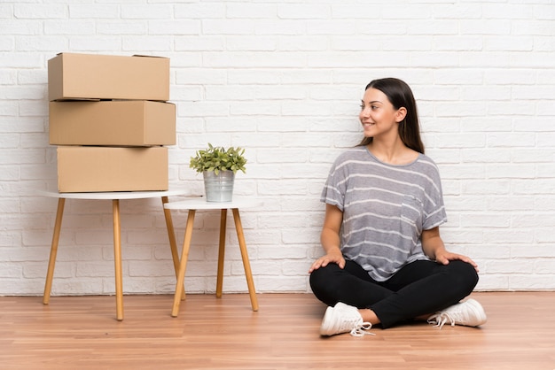 Young woman moving in new home among boxes looking to the side