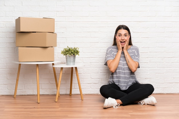 Young woman moving in new home among boxes with surprise facial expression