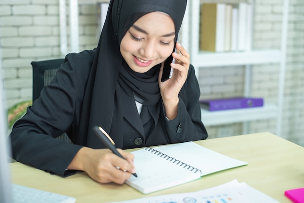 Мусульманская работа молодой женщины в офисе используя телефон