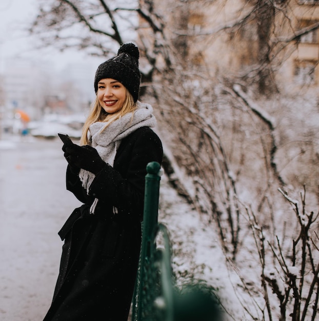 Young woman n warm clothes enjoying in snow and using mobile phone