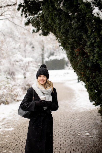 テイクアウトのコーヒー カップと雪の中で楽しんでいる若い女性 n 暖かい服