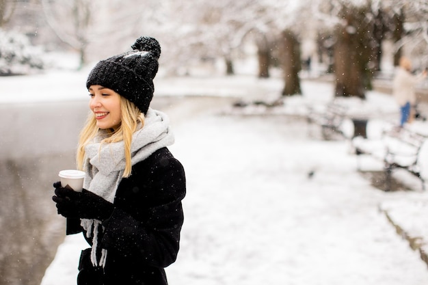 テイクアウトのコーヒー カップと雪の中で楽しんでいる若い女性 n 暖かい服