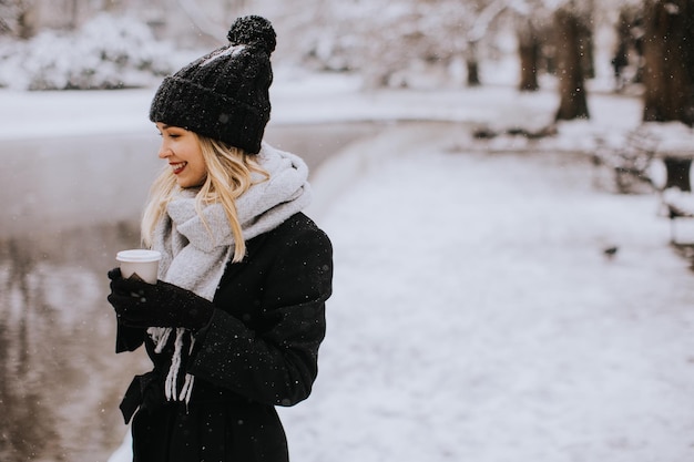 テイクアウトのコーヒー カップと雪の中で楽しんでいる若い女性 n 暖かい服