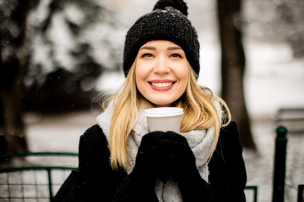 テイクアウトのコーヒー カップと雪の中で楽しんでいる若い女性 n 暖かい服