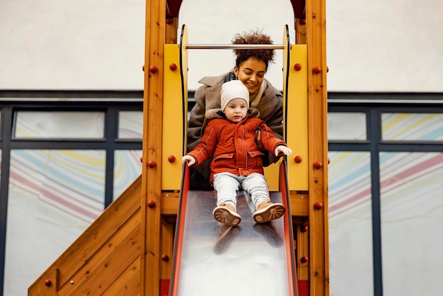 A young woman nanny teaching a little boy how to ride slides at playground