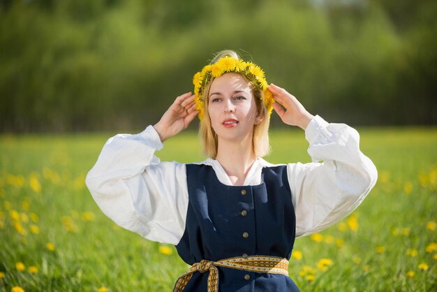 Young woman in national clothes wearing yellow dandelion wreath in spring field ligo