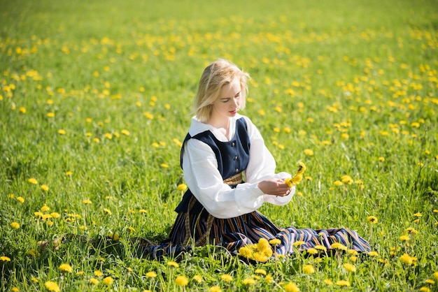 Young woman in national clothes wearing yellow dandelion wreath in spring field springtime