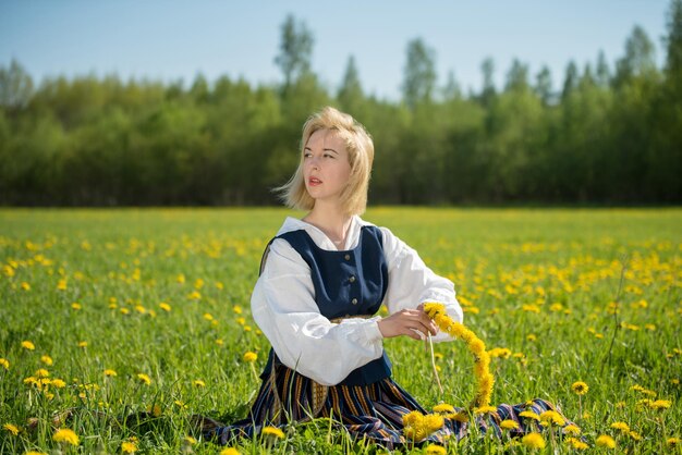 Young woman in national clothes wearing yellow dandelion wreath in spring field springtime