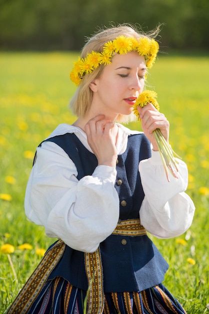 Giovane donna in abiti nazionali che indossa una corona di tarassaco gialla in campo primaverile primavera
