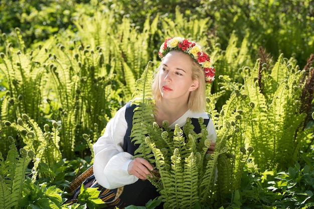 녹색 고사리 리고 라트비아 휴일의 배경에 대해 국가 옷과 화환을 입은 젊은 여성