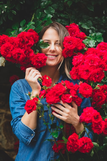 Giovane donna vicino al cespuglio di rose rosse in un giardino