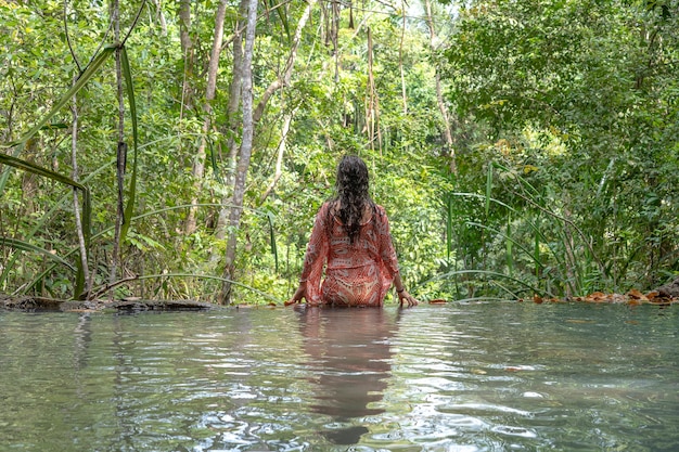 Young woman near turquoise water of cascade waterfall at deep tropical rain forest, island Koh Phangan, Thailand