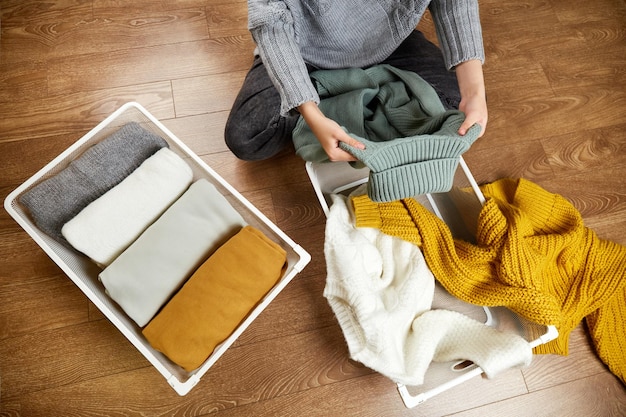 A young woman neatly puts stacks of clothes into a metal laundry basket