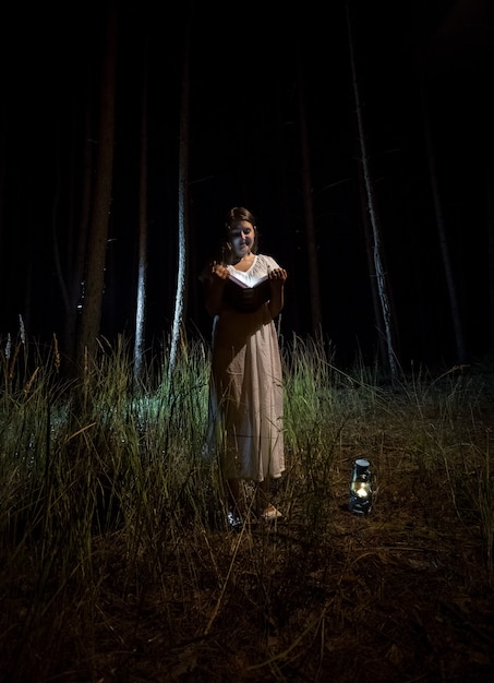 Photo young woman in nightgown reading book at night forest