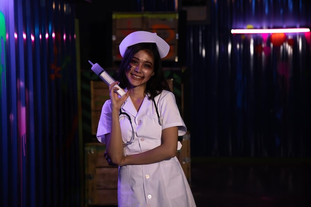 Young woman in nurse costume holding syringe and stethoscope with blood at Halloween party.